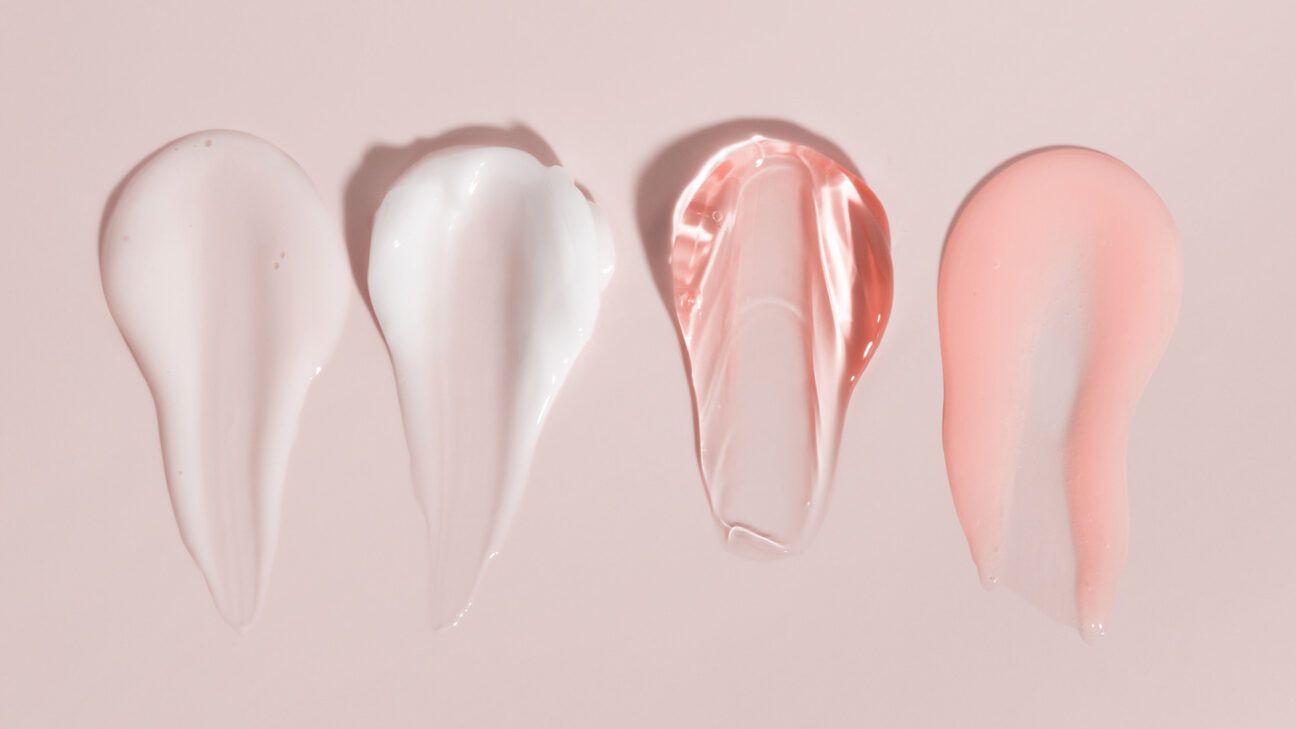 Four dollops of face creams are seen on a pink background.