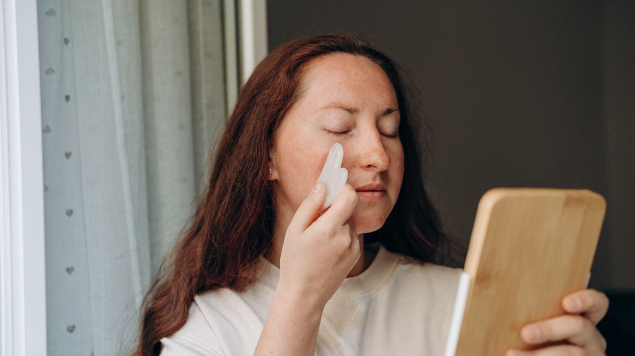 A woman practicing facial gua sha massage for headache relief. 