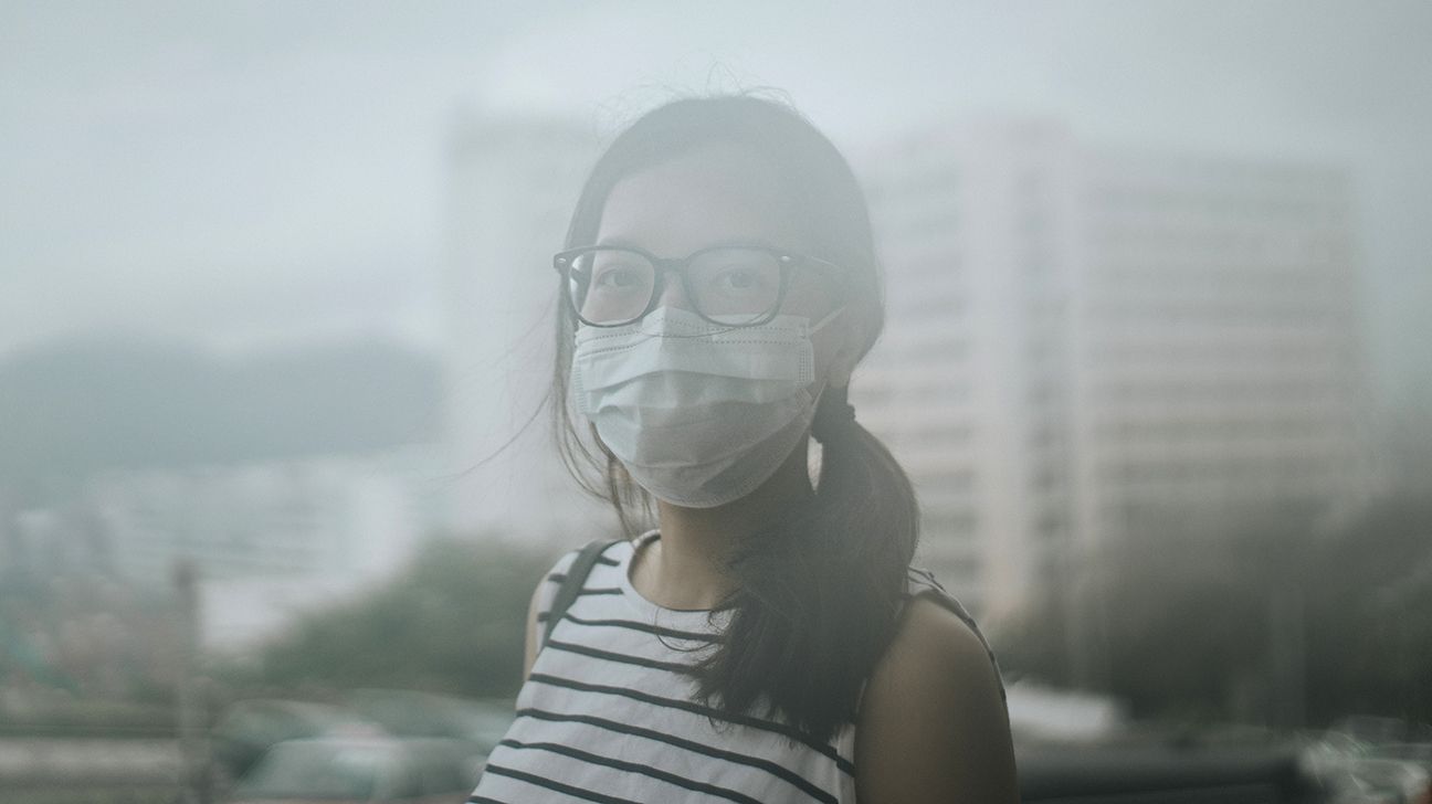 A young Asian woman wearing a face mask outdoors during heavy air pollution.