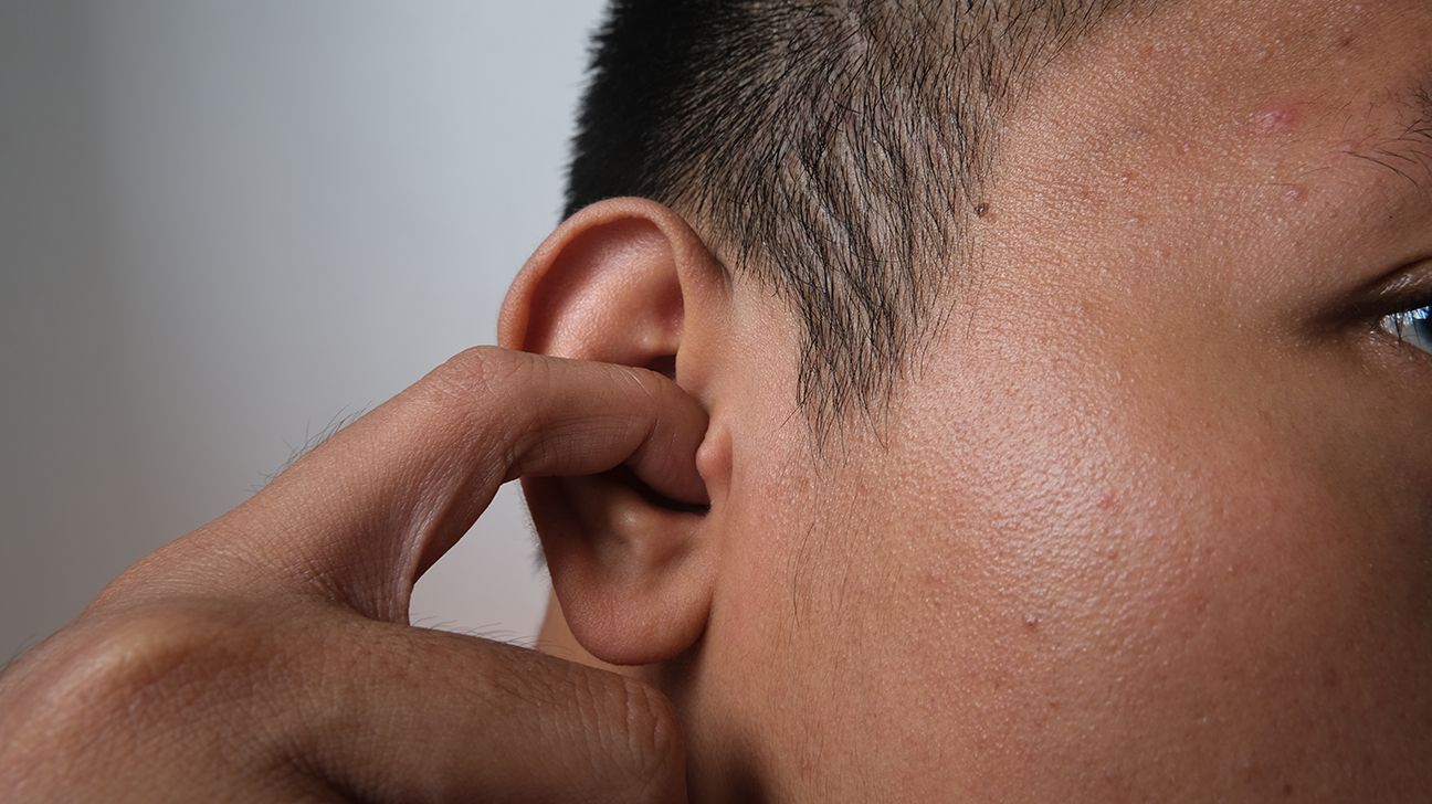 Close-up of man with his finger placed inside his ear scratching, to depict dry ears.