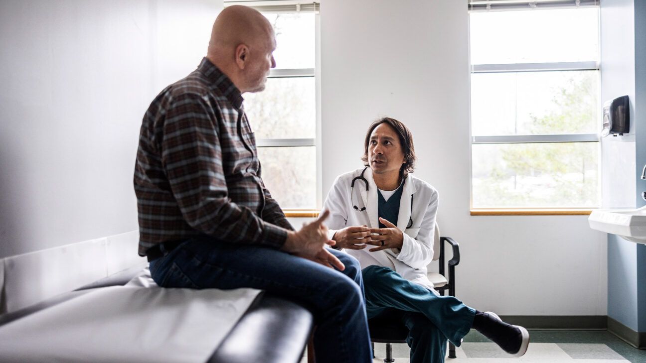 Male patient speaks with physician in exam room.