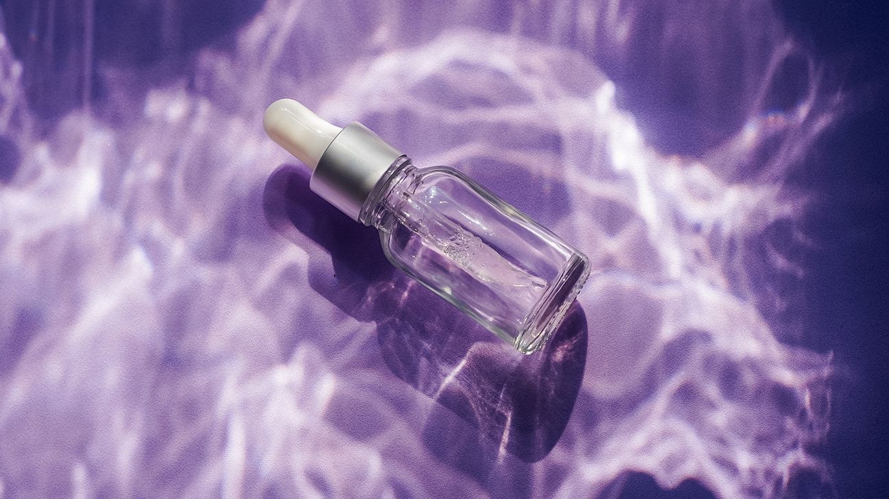 Glass bottle of lavender oil on a purple background.