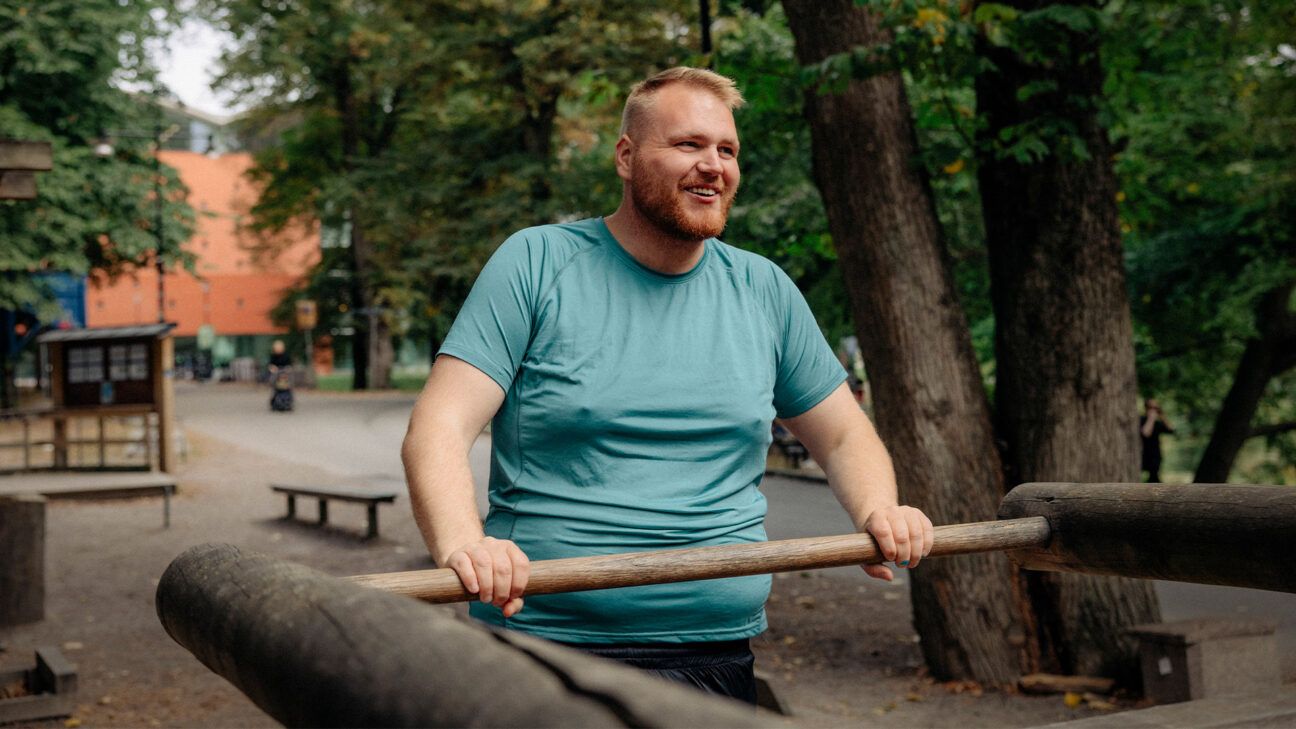 Man in green shirt is seen smiling in a park.