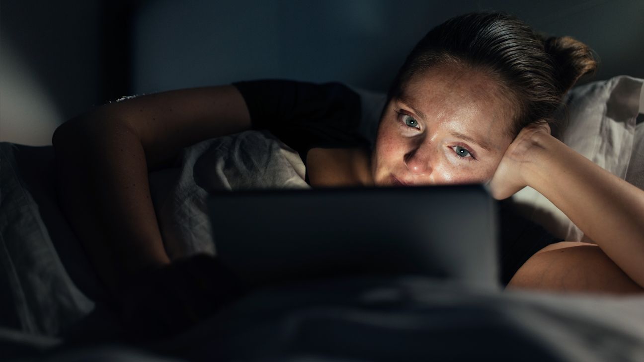 Woman in bed looks at tablet at night.