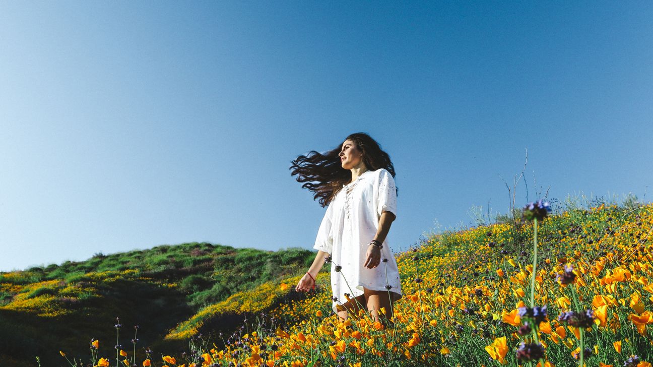 Female in white dress standing in field of orange daffodils. 