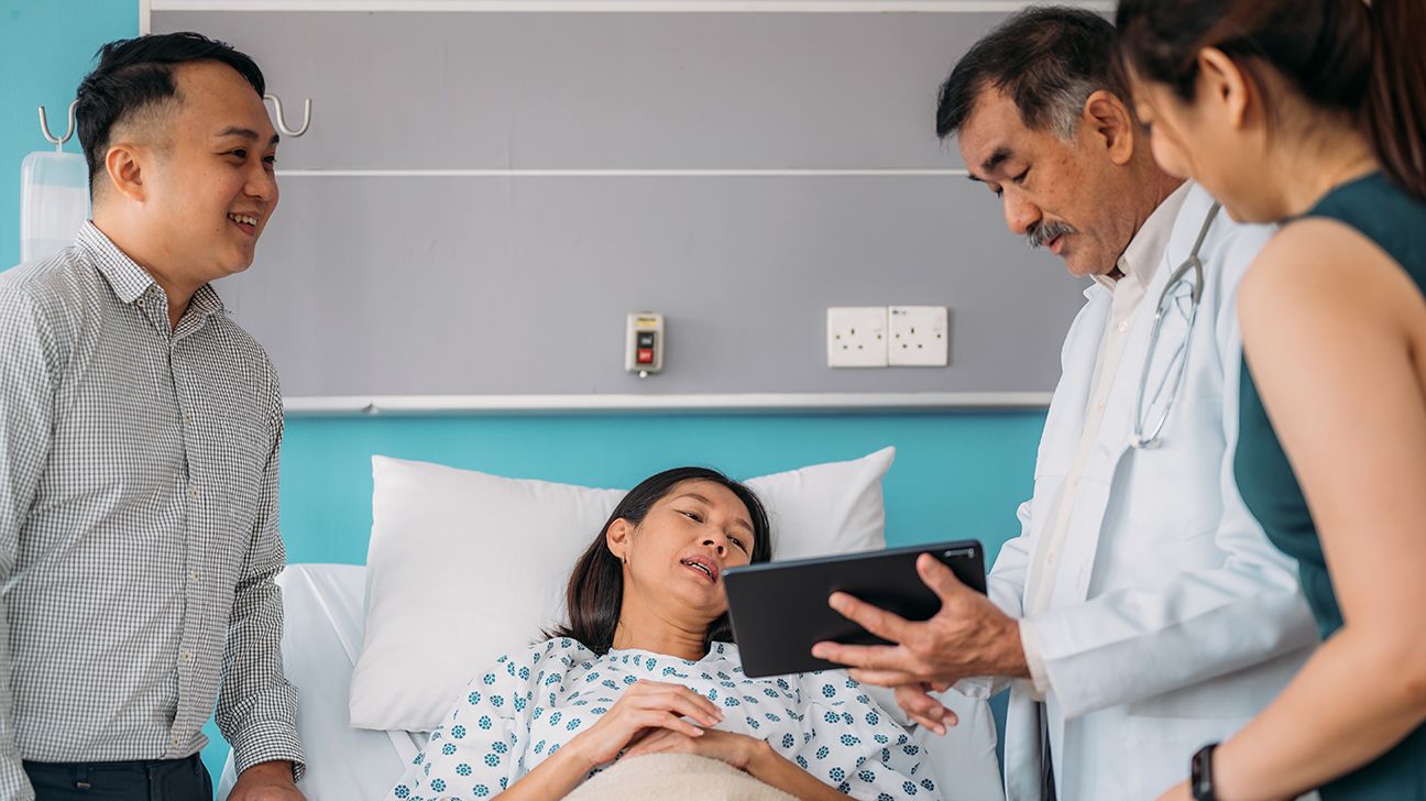 Doctor speaking with a patient surrounded by their family as they lay in a hospital bed. 