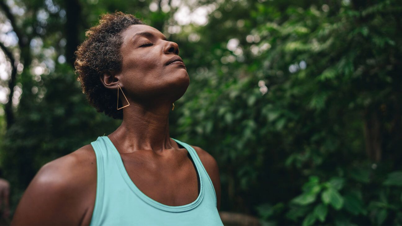 Woman in blue tank top seen outdoors with eyes closed.