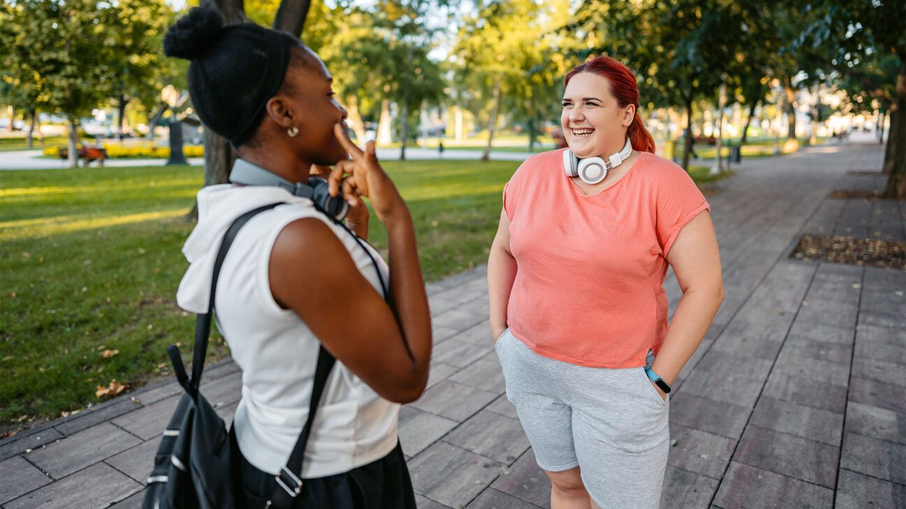 Woman in pink shirt talks to woman in a white shirt outside in a park.