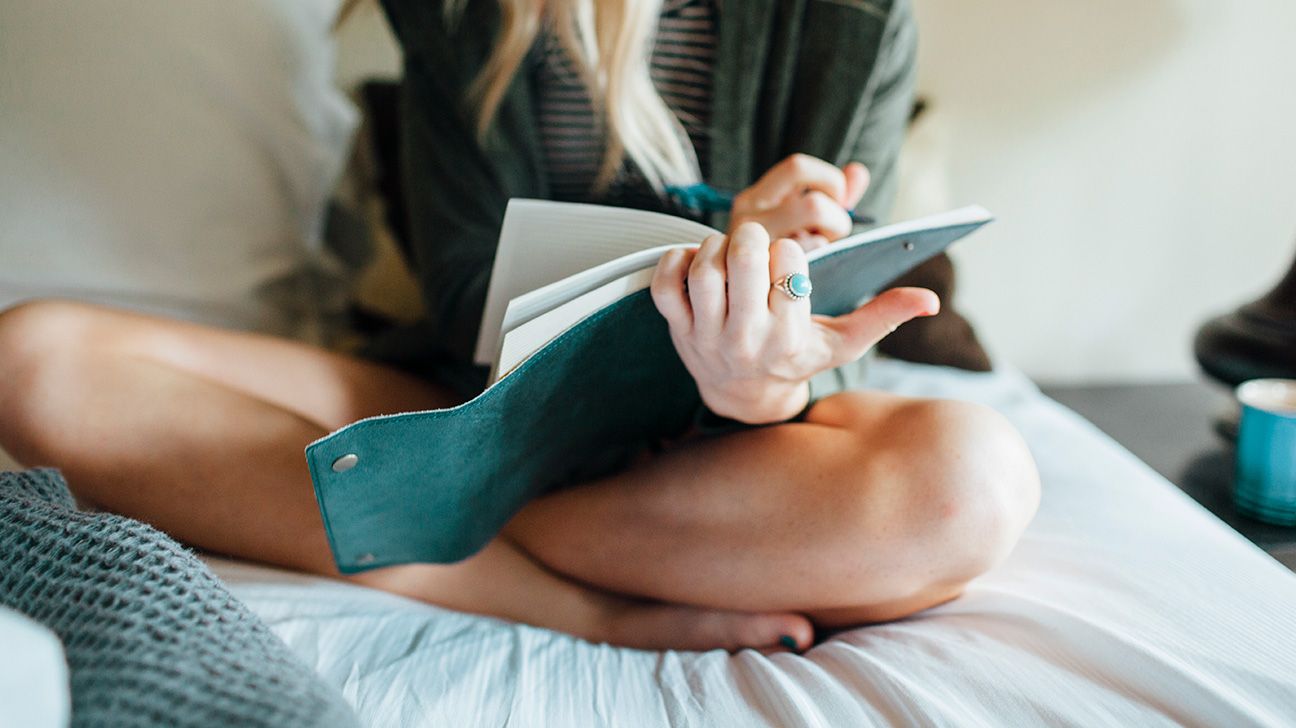 woman writing in a journal while sitting on a bed
