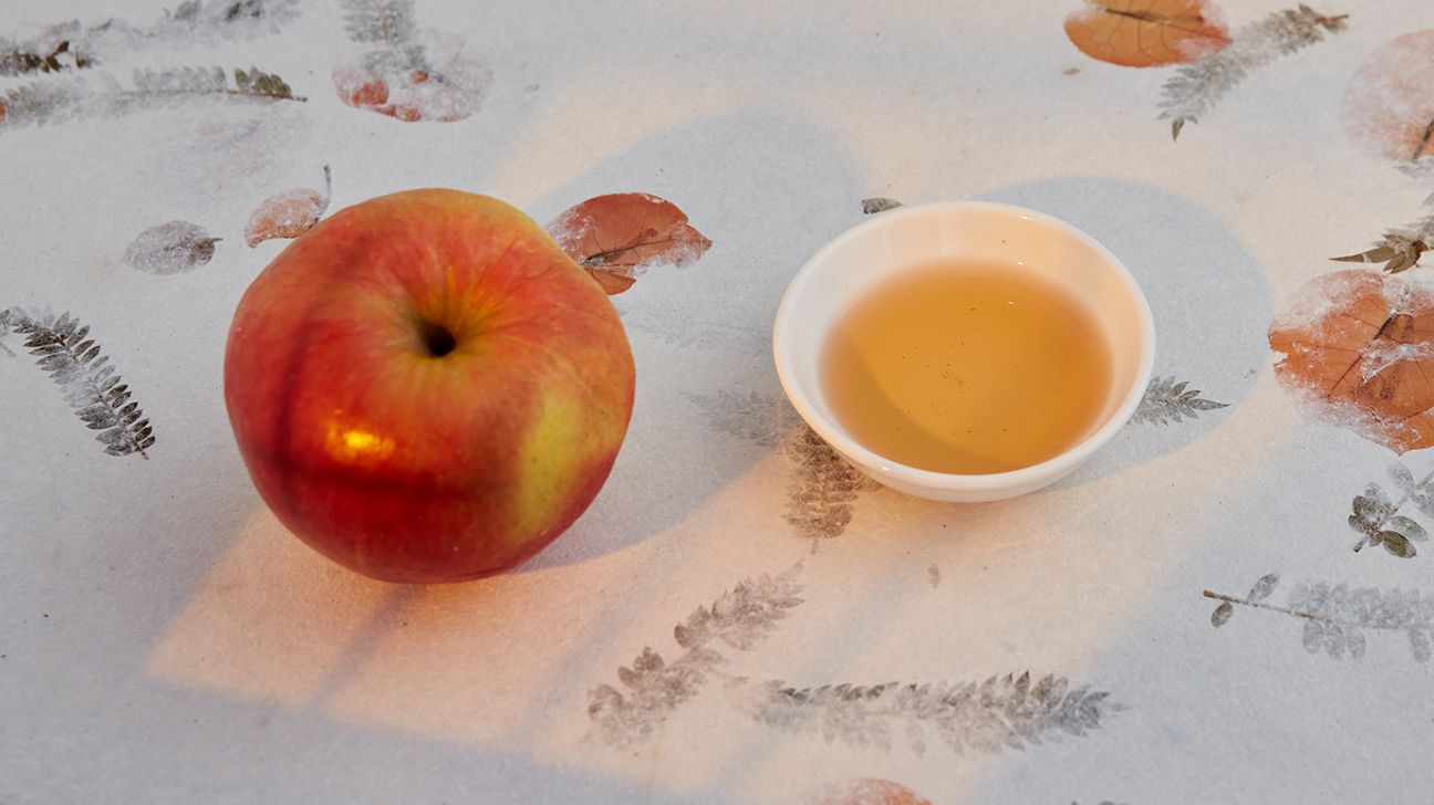 Apple next to dish of apple cider vinegar on table