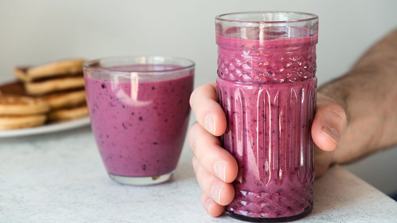 A hand is holding a blueberry protein shake