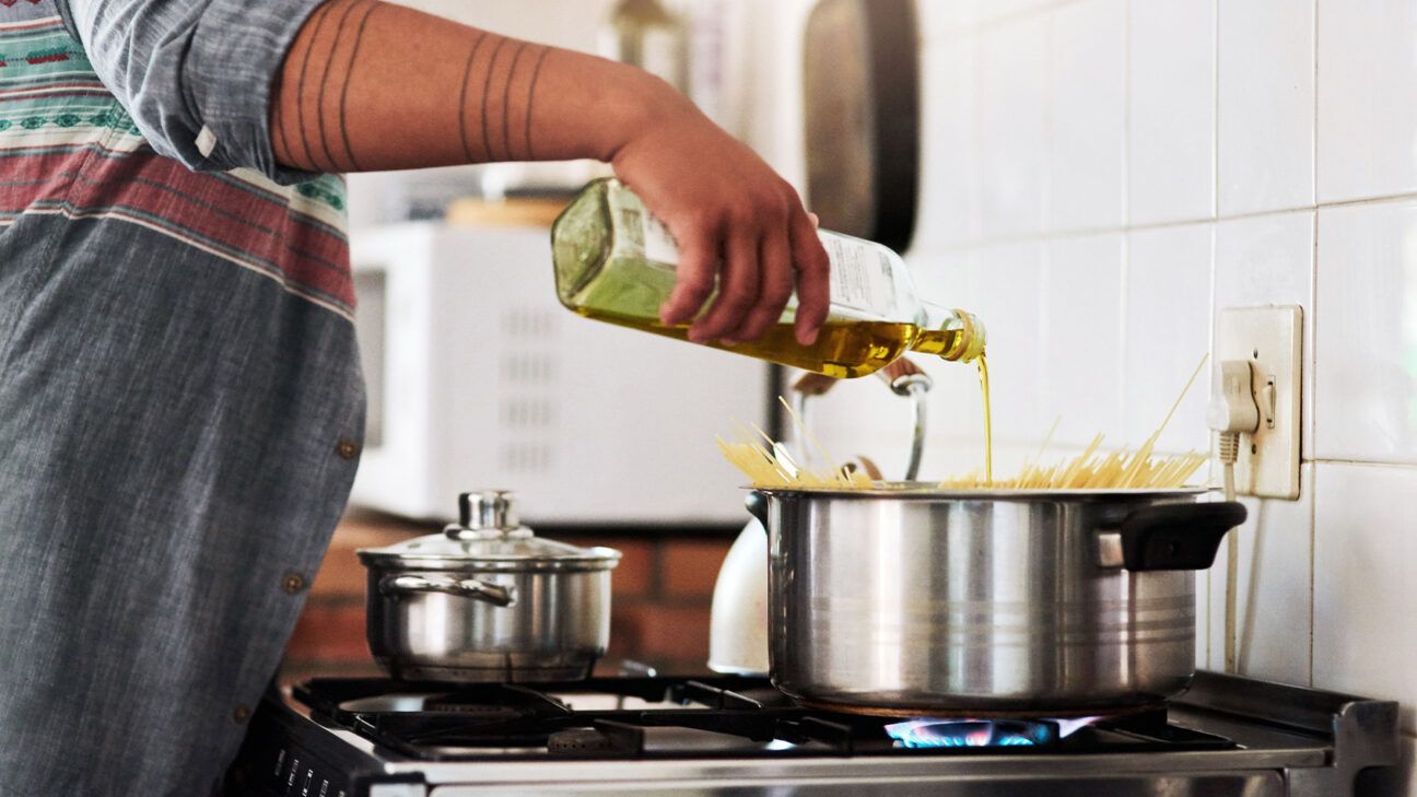 A person pours olive oil into a pot on a stove.