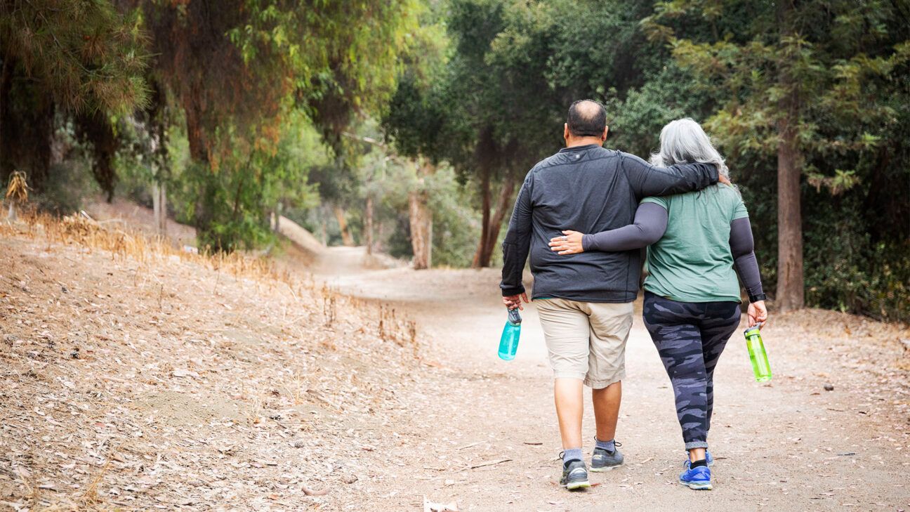 Man and woman walk arm in arm on a trail.
