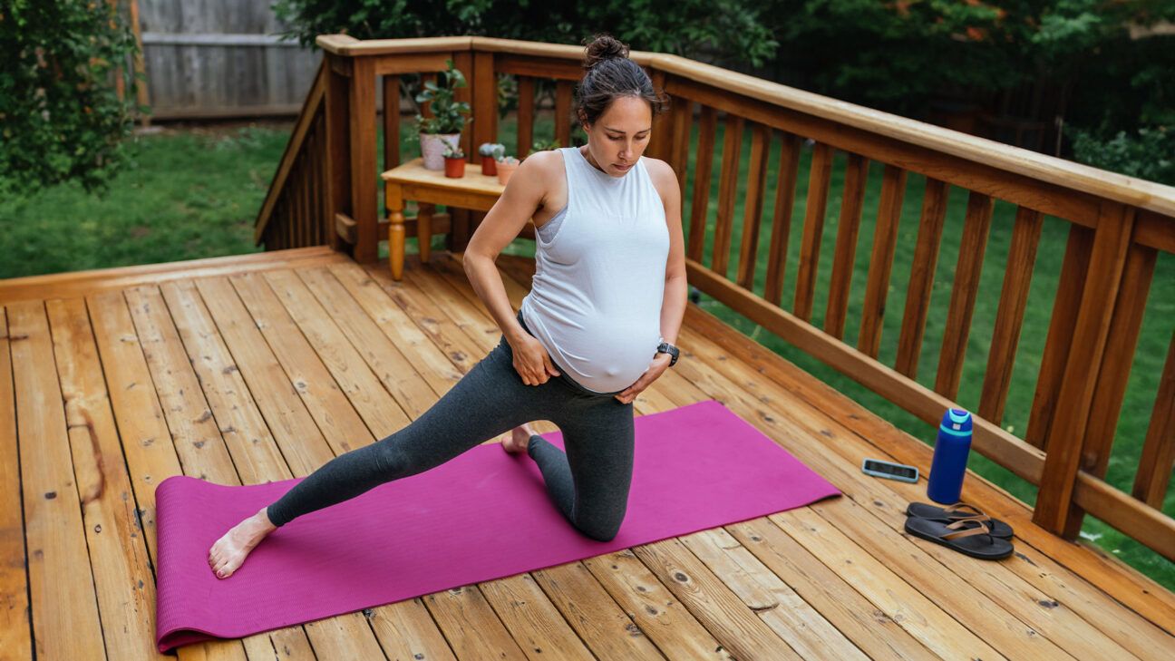 Pregnant woman does yoga on a pink yoga mat.