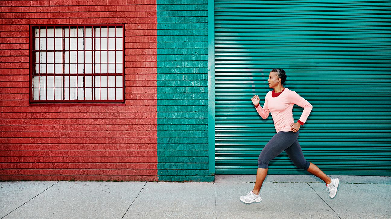 Woman jogging on a city street in front of a colorful wall