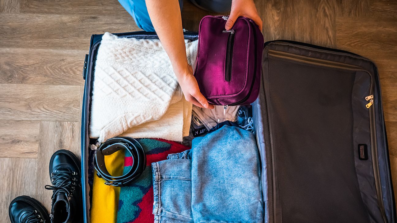 person packing clothes and toiletries bag in suitcase