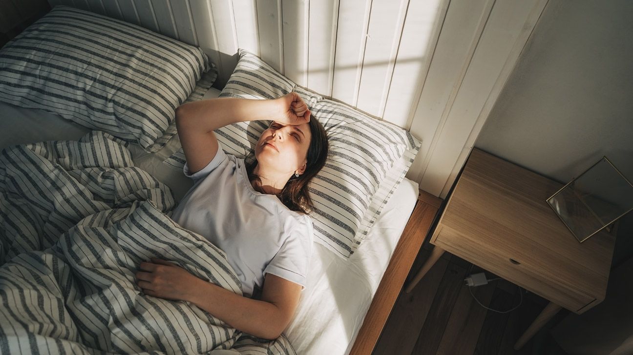 Female lying in bed with her hand over her head to depict being unable to sleep.