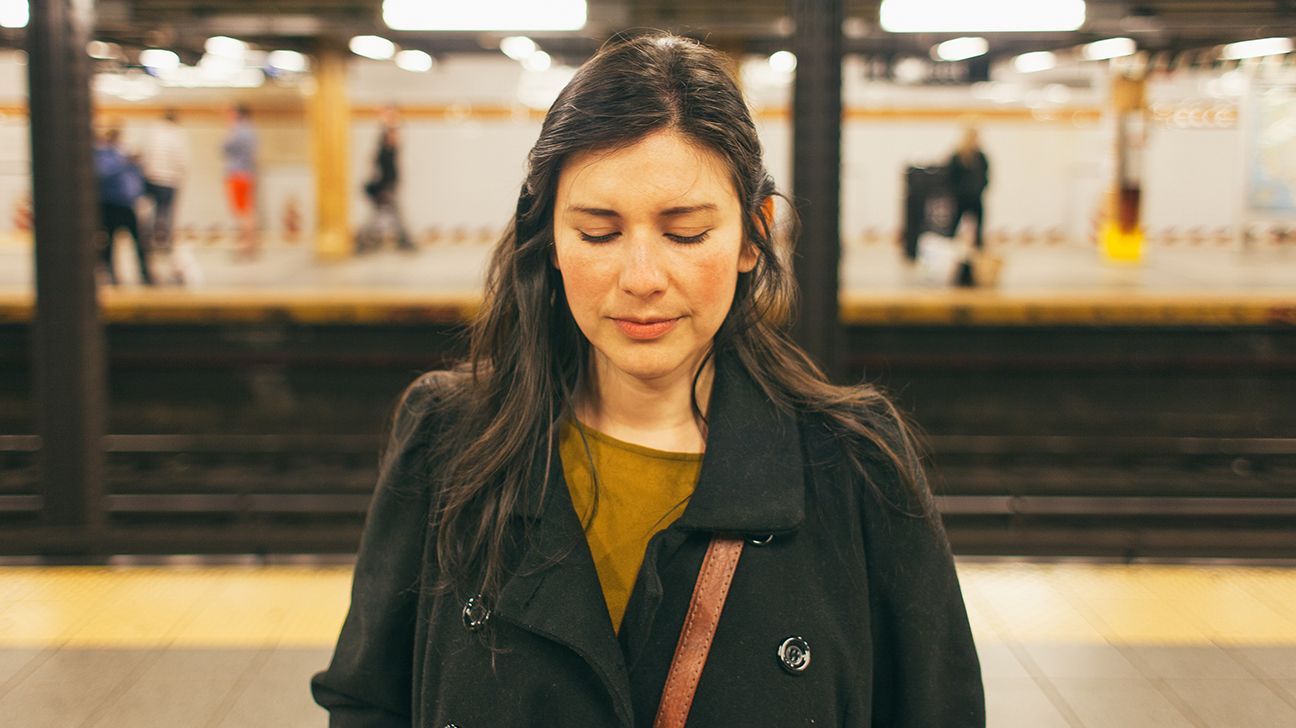 Female wearing a black trench coat standing at the subway station.