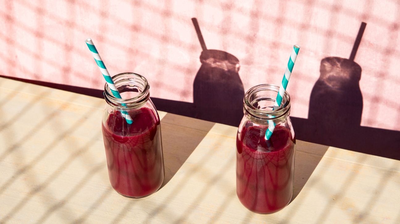 Two bottles of beet juice with a blue and white straw are seen on a table.