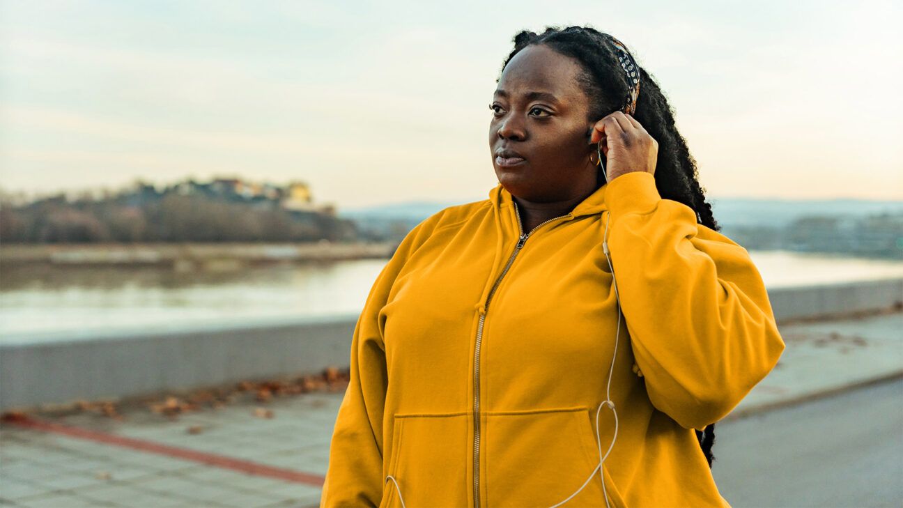 Woman in yellow jacket puts in headphones.