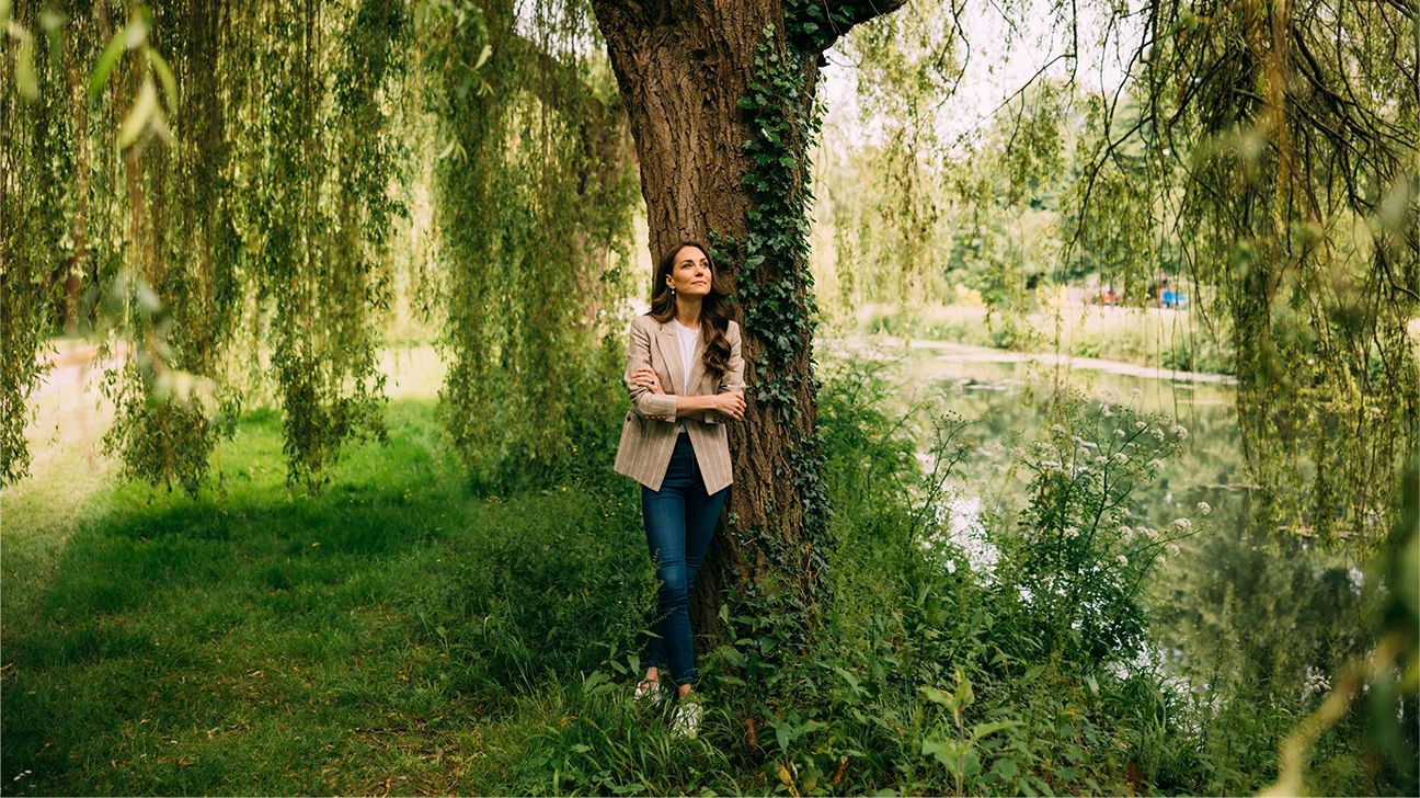 Kate Middleton is seen standing outdoors by a large tree.