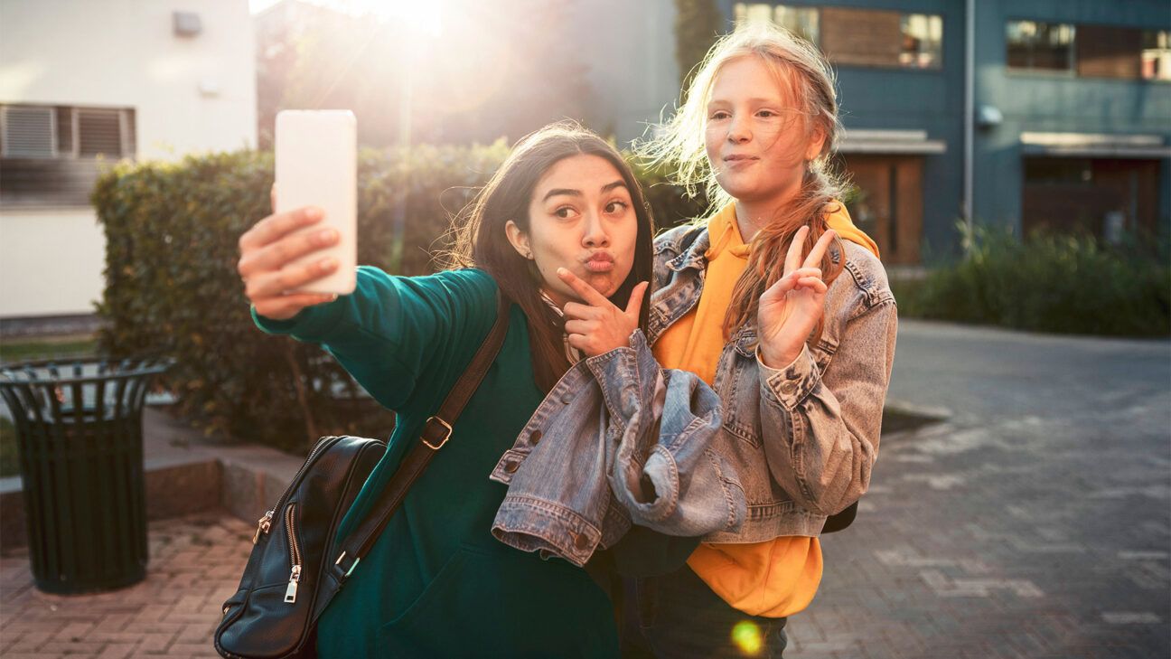 Two teen girls take a selfie with a smart phone.