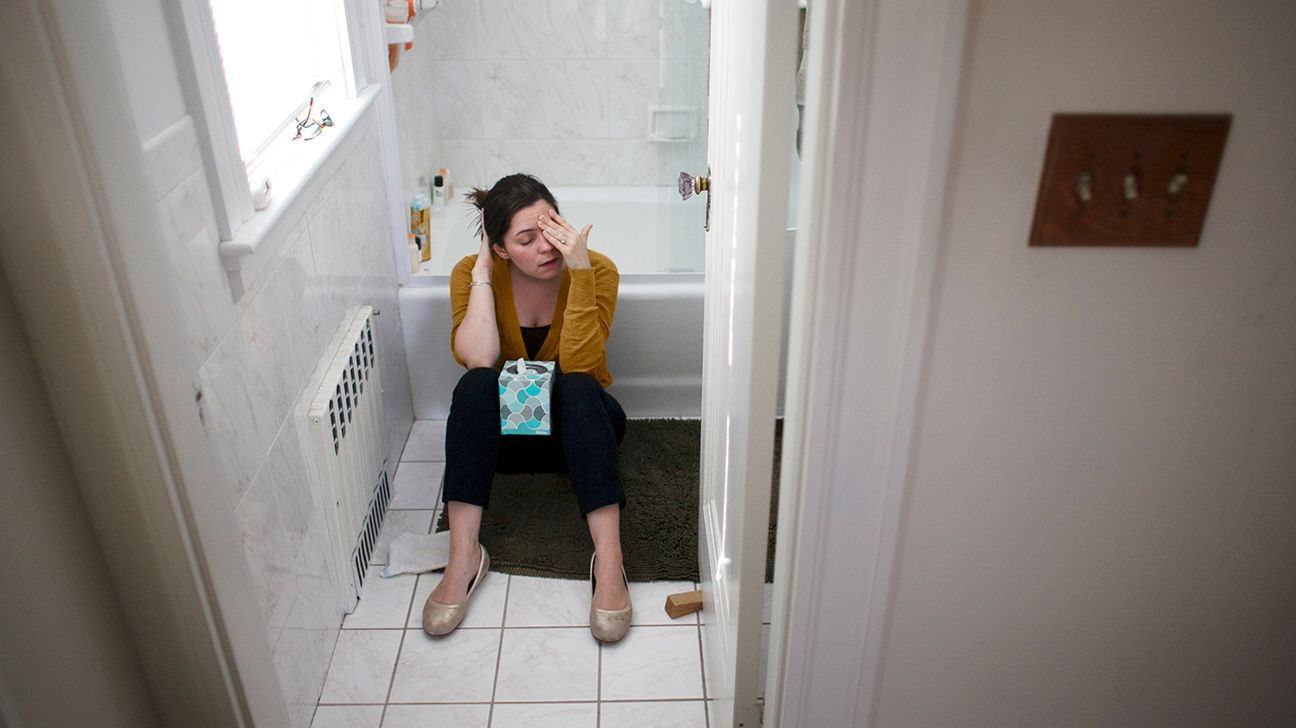 woman sitting on bathroom floor with box of tissues looking nauseous