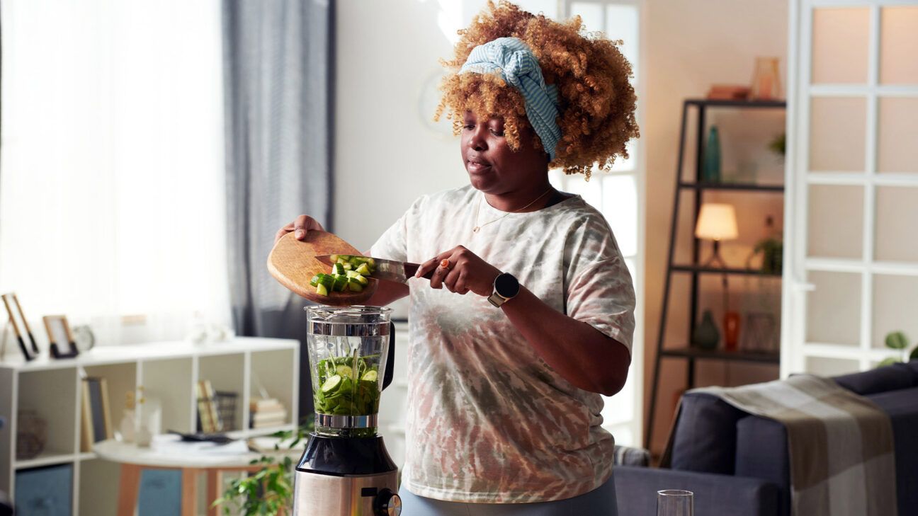 Female putting vegetables in a blender.