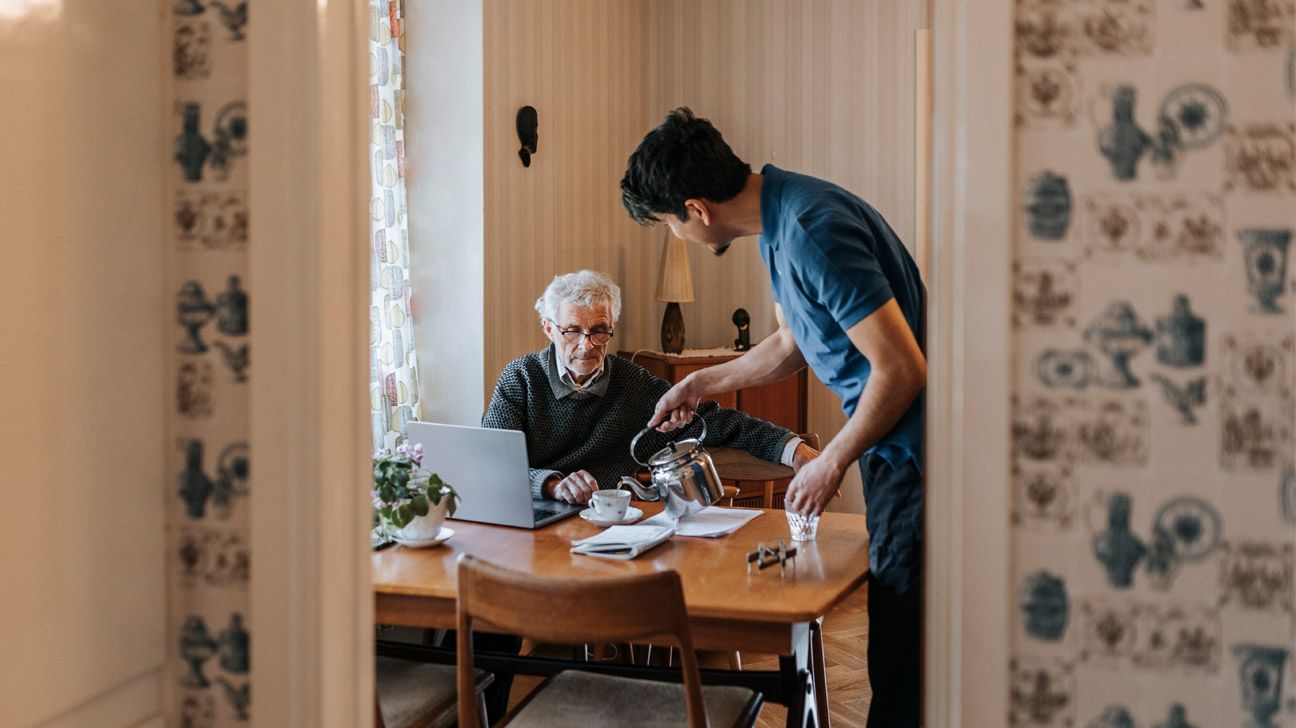 A male caregiver pours tea for a male patient