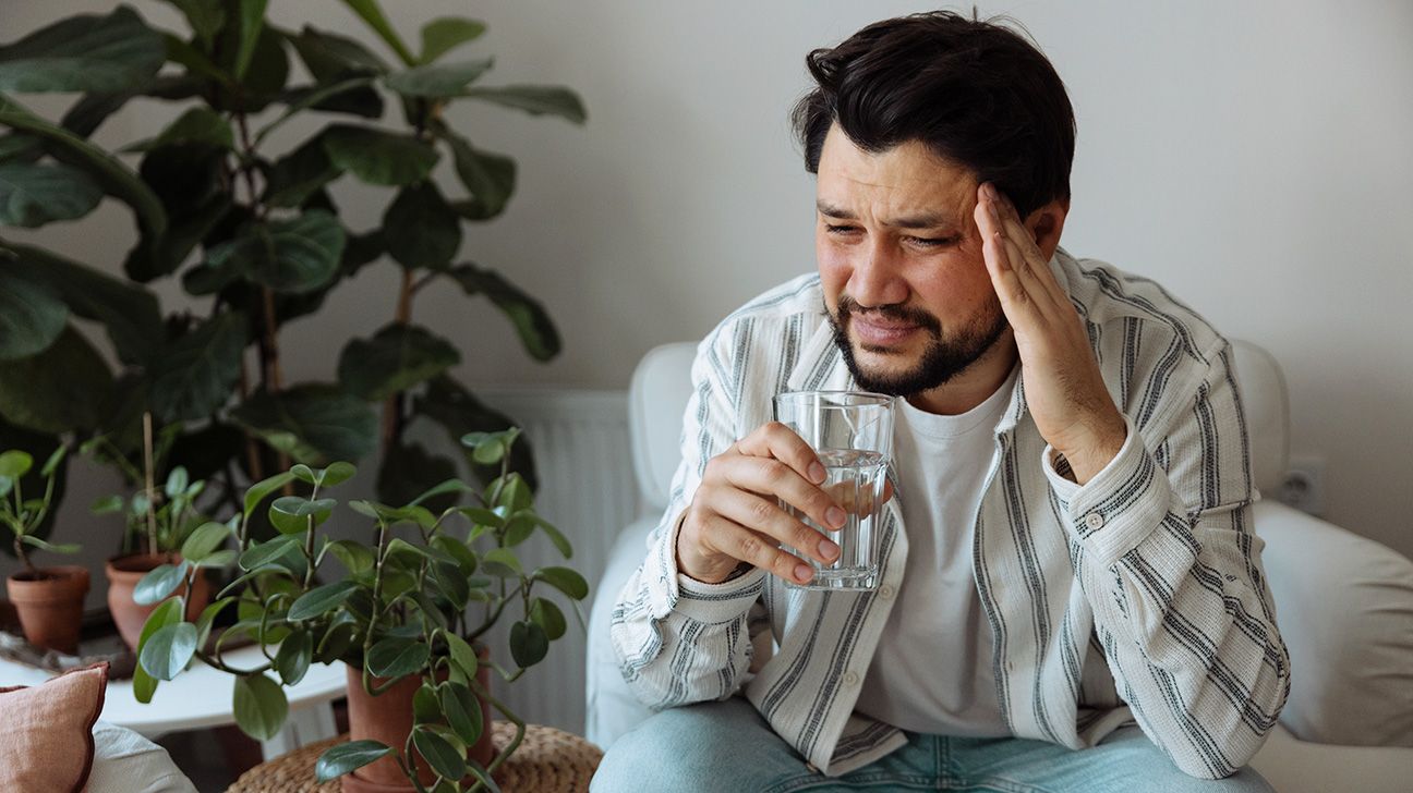 A man with a headache drinks water to hydrate