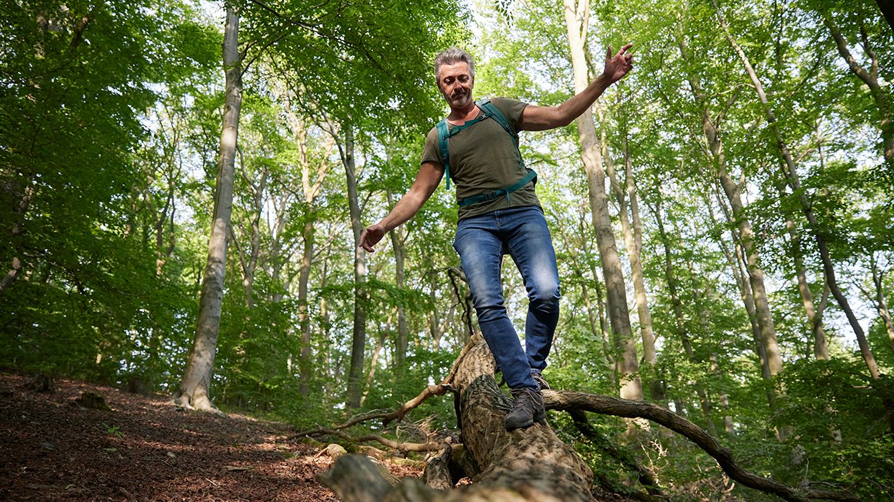 A man balancing on a log during a hike. 