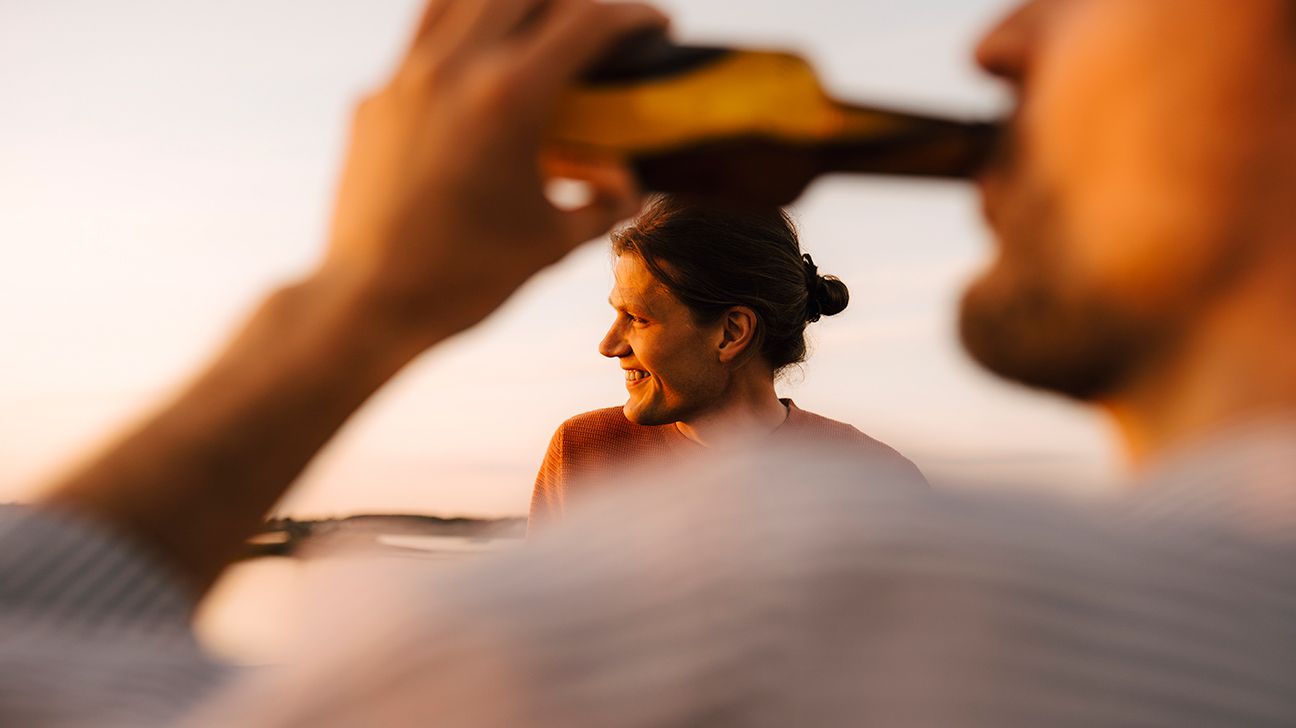 Man drinking beer with woman in background