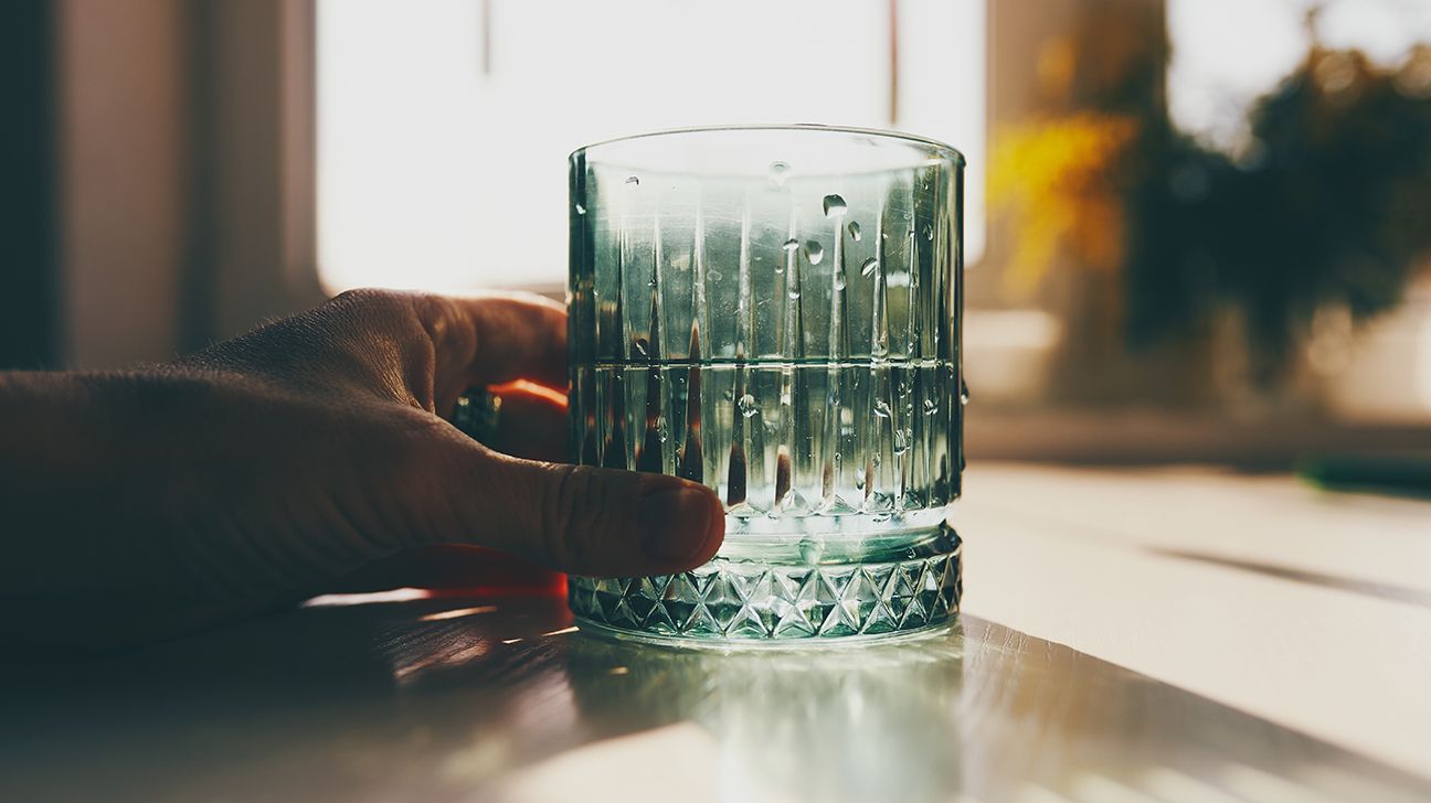 hand holding textured glass of water with sunlight reflecting