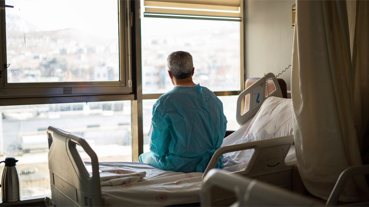 Male with cancer sits on hospital bed by the window