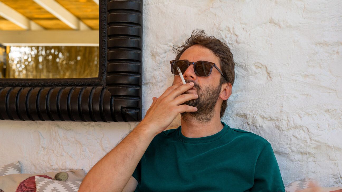 Male leans against a wall smoking