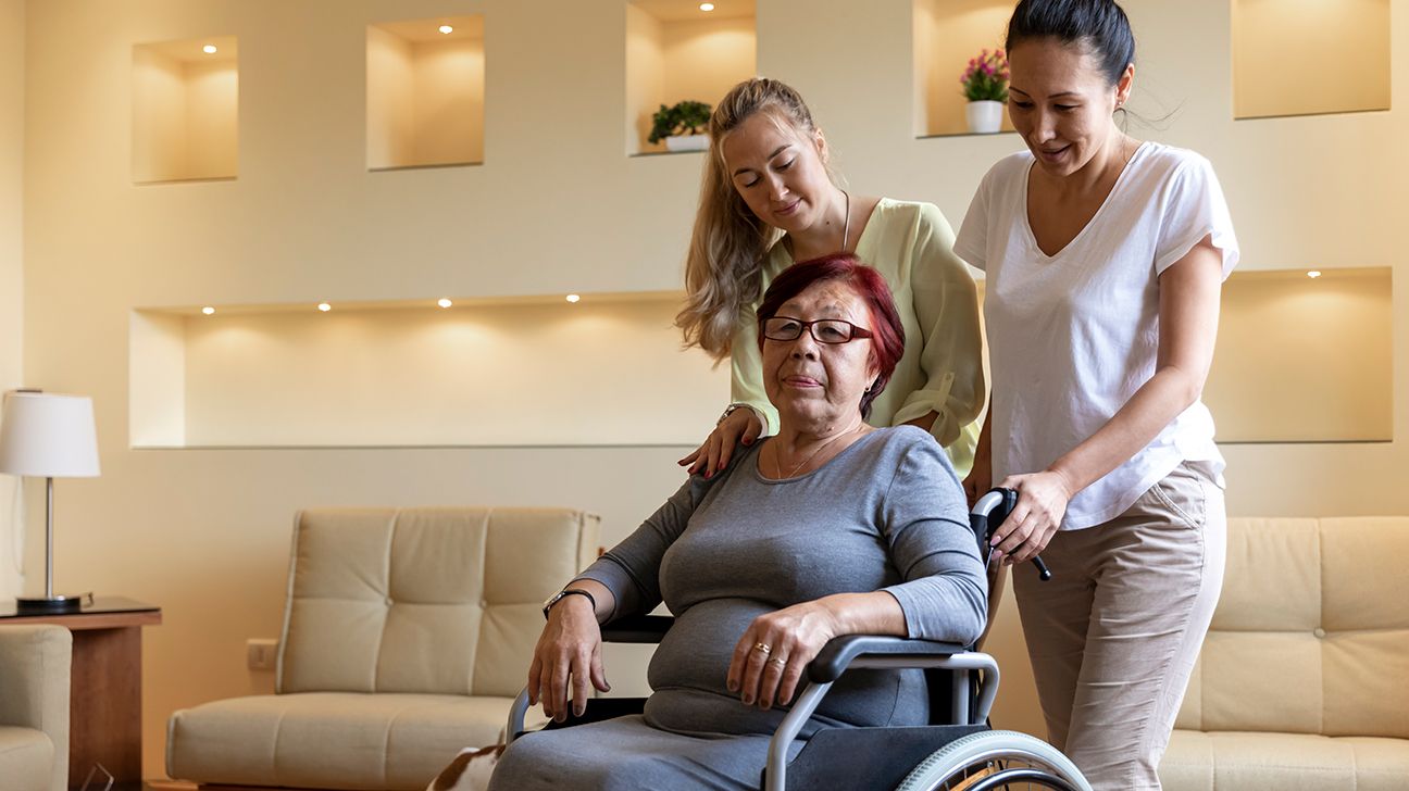 An older woman in a wheelchair is taken care of by two daughters