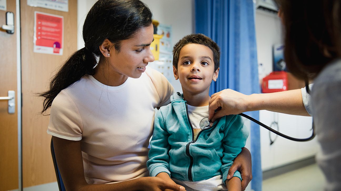 parent sitting with their child in a medical office as a doctor listens to their chest with a stethoscope