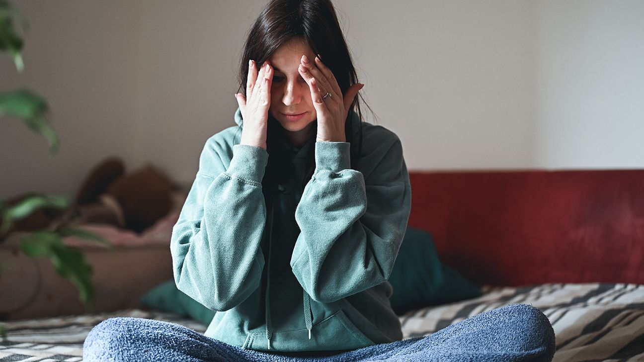 person with viral meningitis sitting on a bed holding their head-1