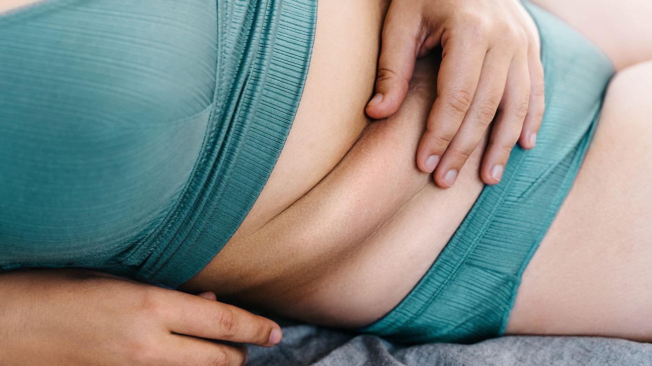 darker-skinned person in bra and underwear pinching folds of skin on exposed abdomen