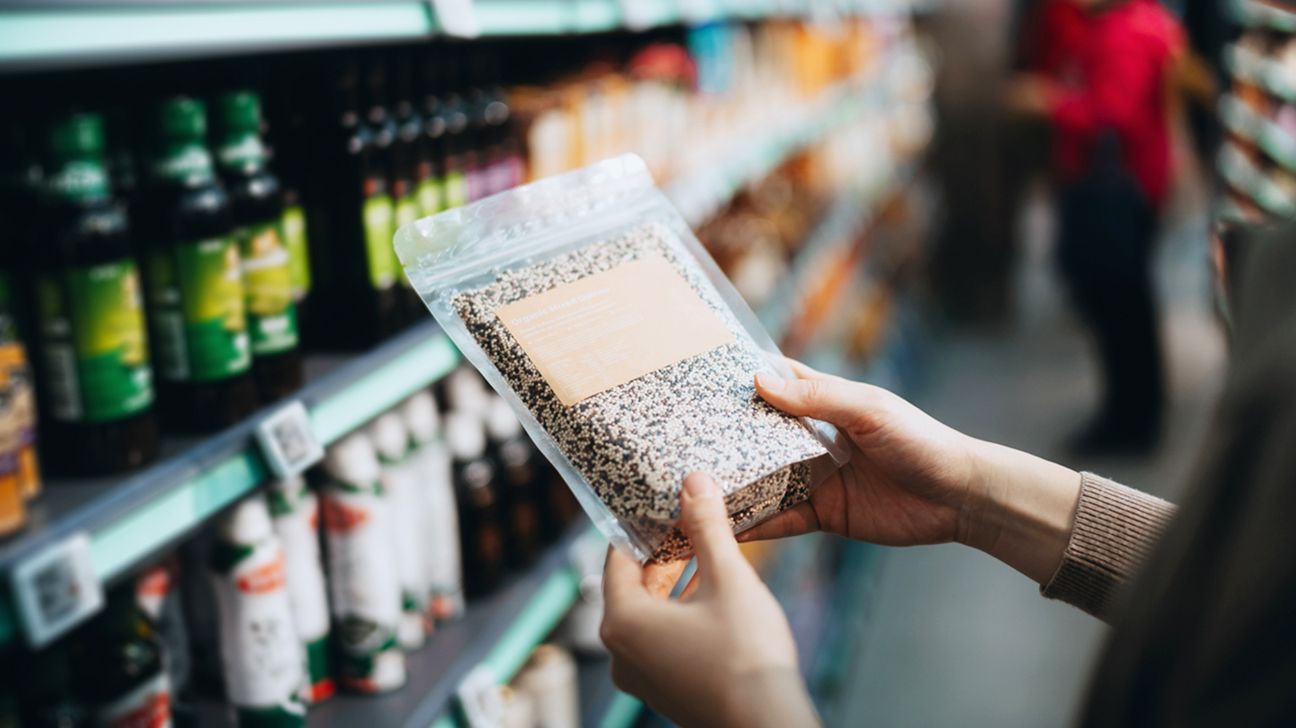 A woman goes grocery shopping and looks at a package of quinoa