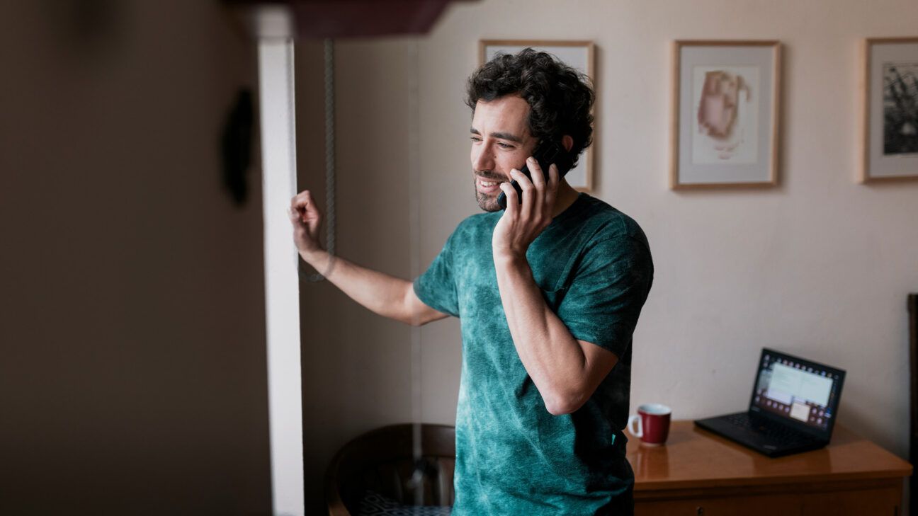 A man wearing a tshirt talks on a mobile phone inside a home