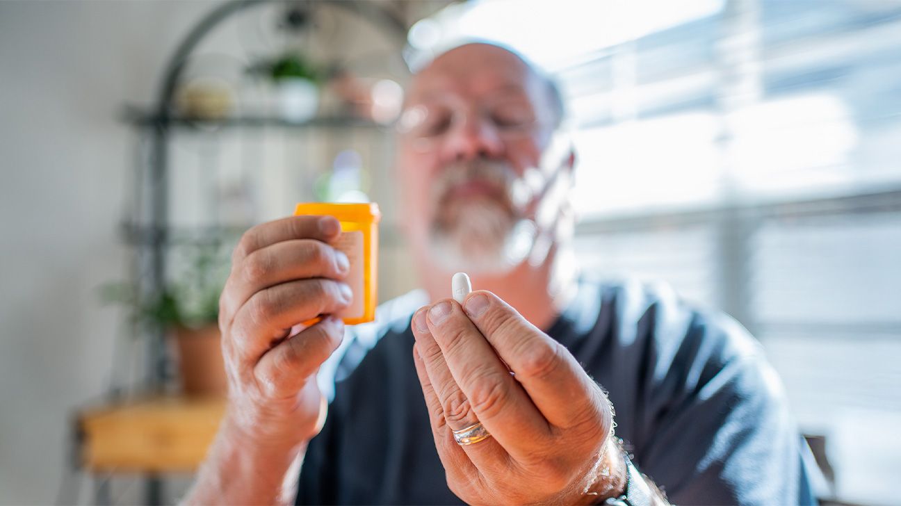 light-skinned man gazing at a tablet held in the fingertips of one hand while holding an opened pill bottle in the other