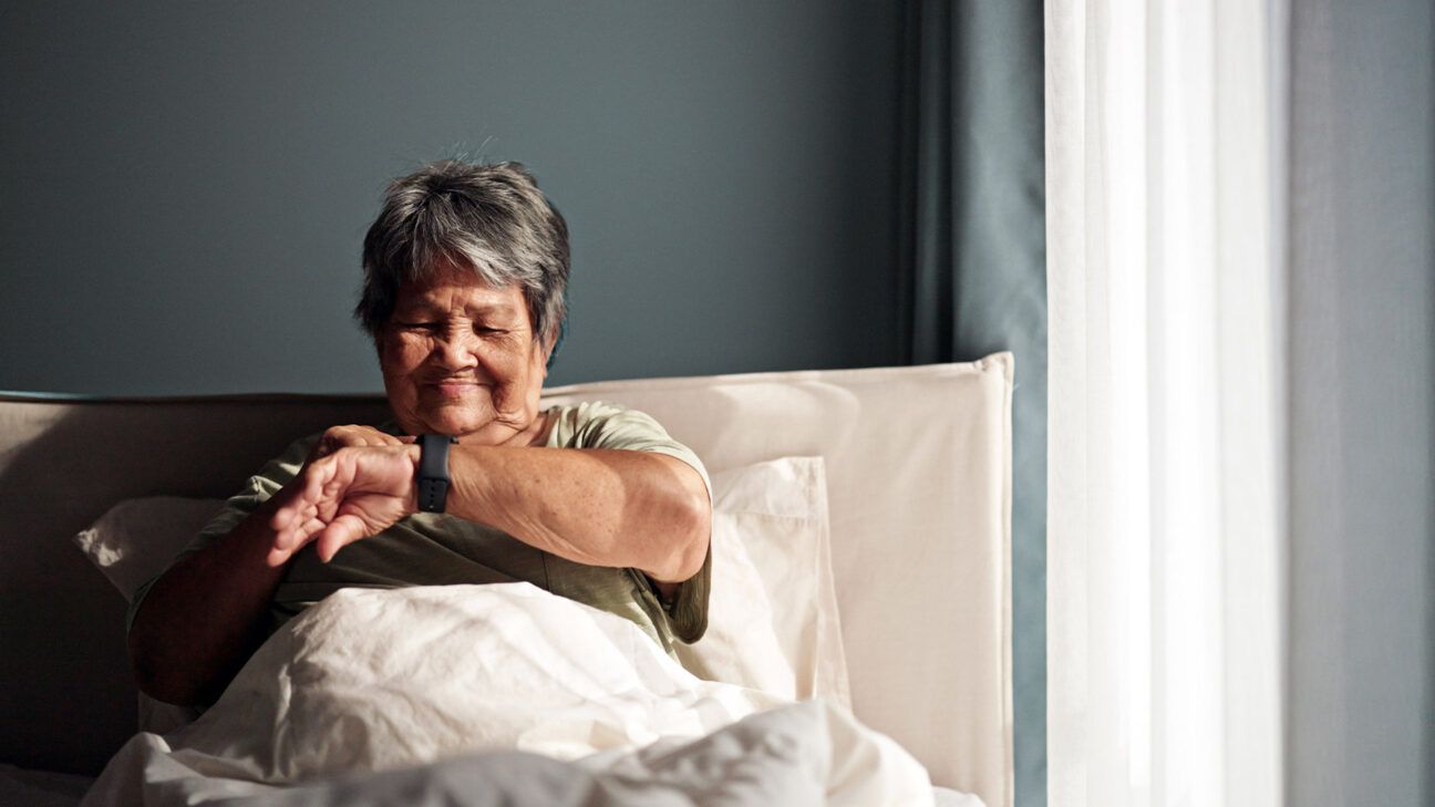 Older female lying in bed looking at a smartwatch.