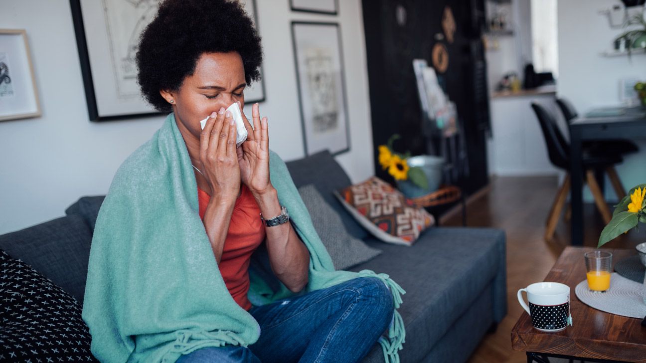 woman-feeling-unwell-at-home-on-couch-drinking-warm-liquid