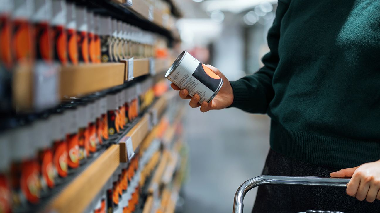 A woman grocery shopping looks at a canned product