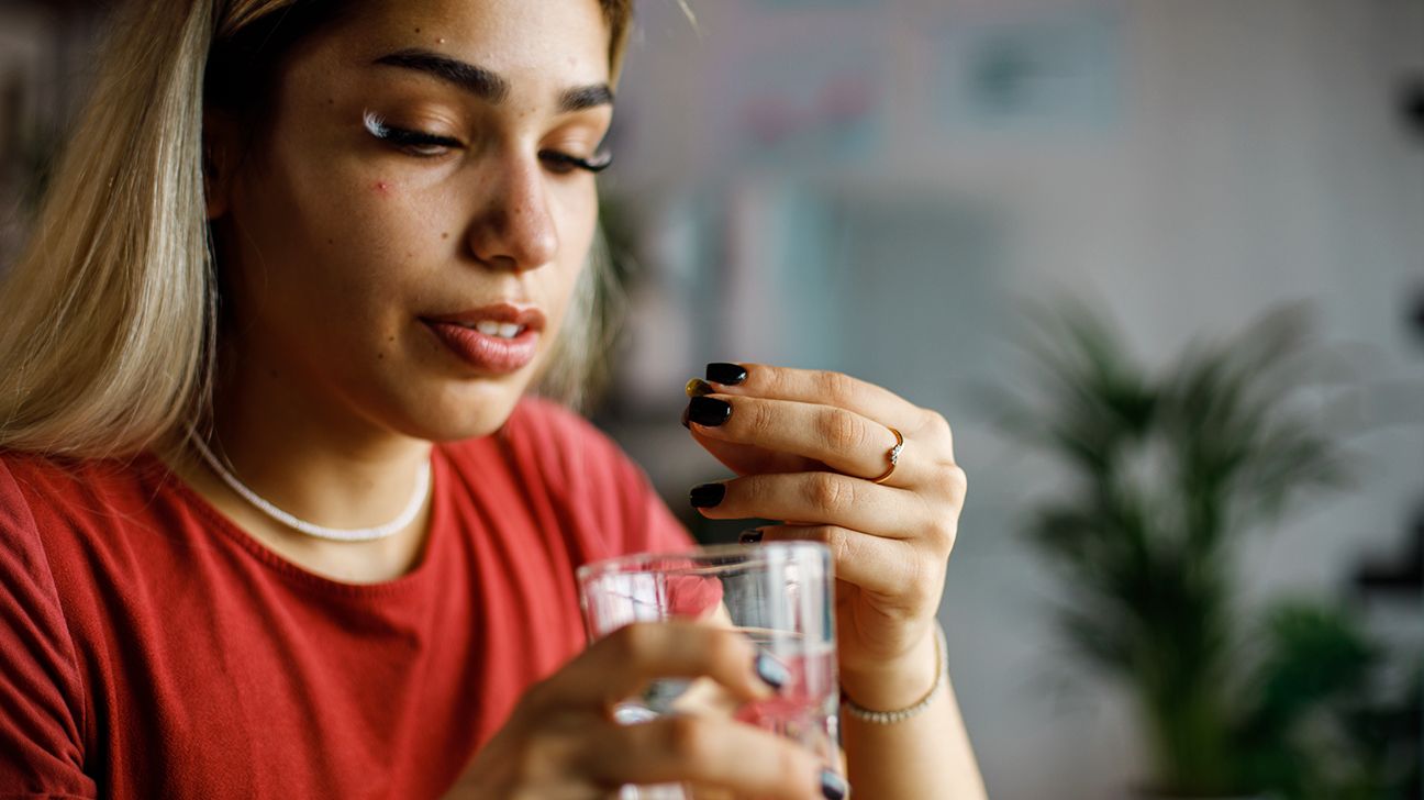 A young woman takes a pill with some water