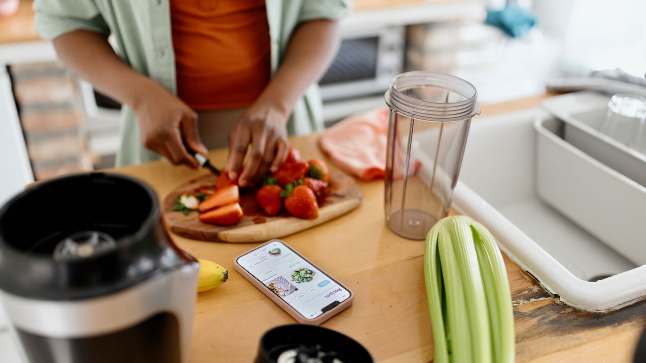 A person preps strawberries for a smoothie in their kitchen