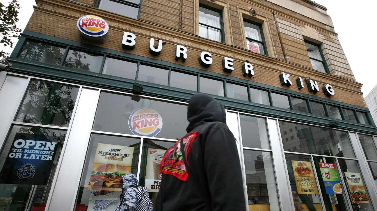 A person in a hoodie walking outside a Burger King.