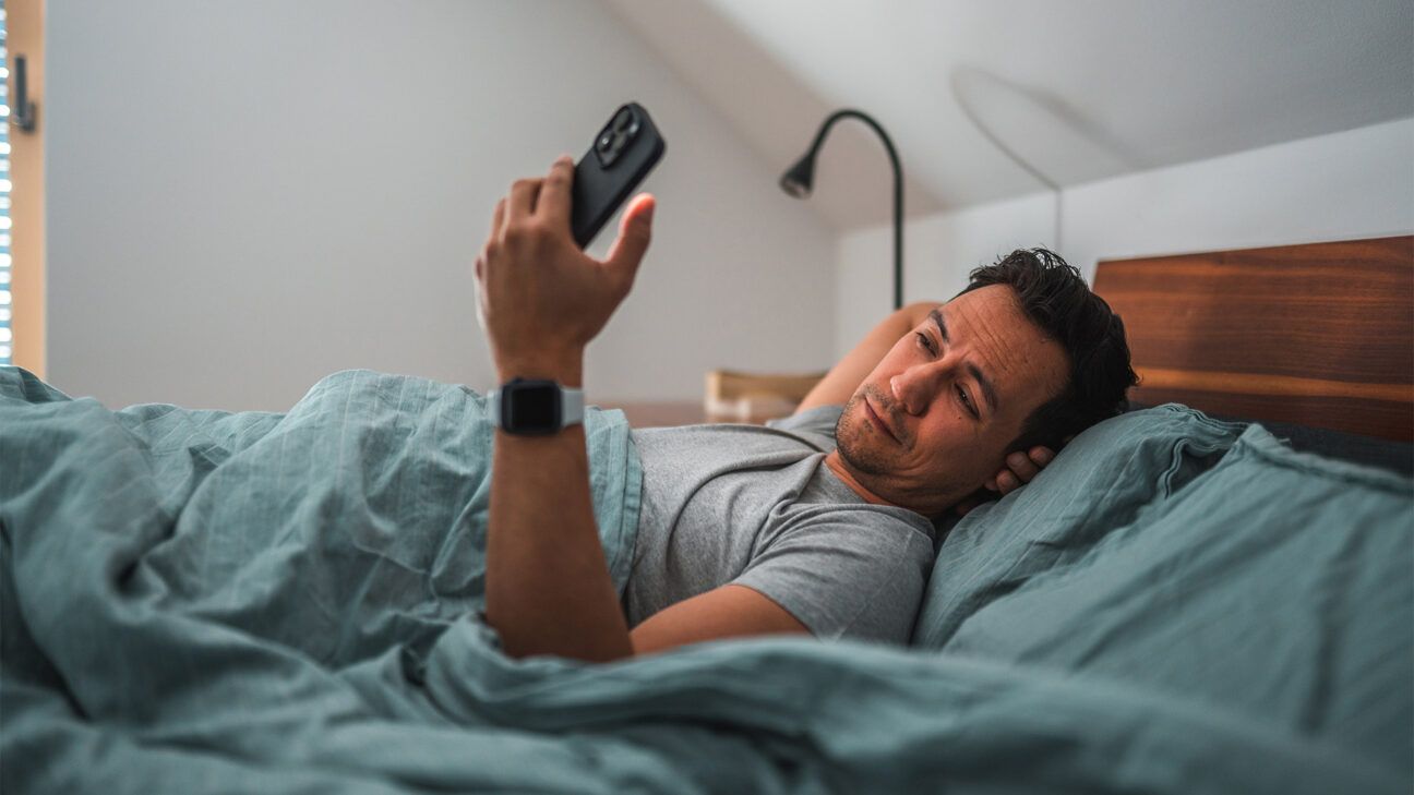 Male looking at smartphone in bed