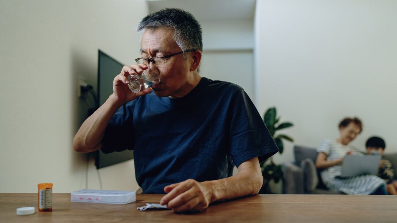 An older male taking medication with a glass of water.